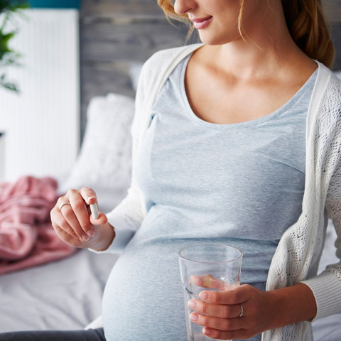 Image of a pregnant woman holding a pill and a glass of water.