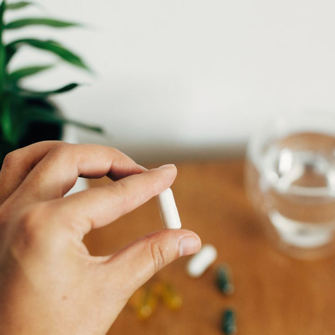 A person holding a magnesium pill in front of a glass of water.