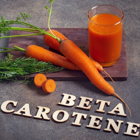Carrot juice, carrots, and the word "beta carotene" on a table.