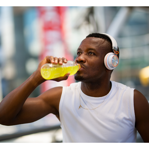 A man with headphones, drinking from a bottle to rehydrate electrolytes.