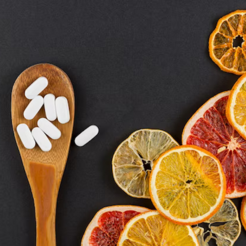 Orange slices and vitamin C tablets in a wooden spoon on a black background.