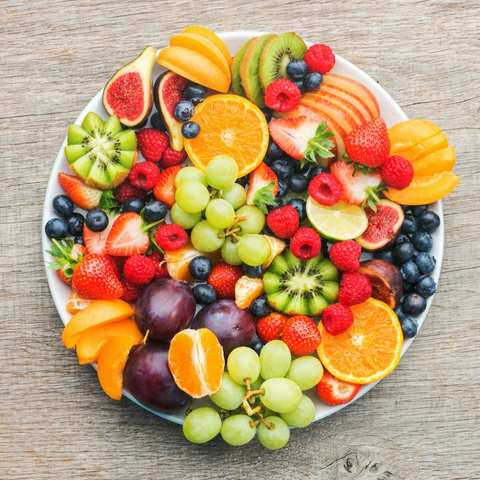 A plate of fresh fruit on a wooden table. Includes kiwi, strawberries, oranges, raspberries, grapes, blackberries, and more.