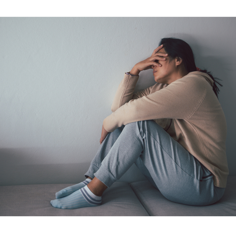 A depressed woman, sitting on a sofa with a hand on her head, covering her eyes.