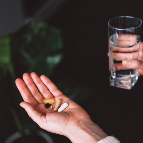 Person holding a glass of water and various iron supplement pills.