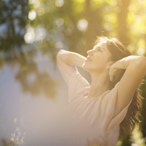 Woman standing in the sun with arms raised, absorbing vitamin D.