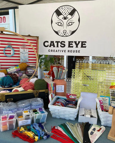 A table filled with curated craft supplies and a banner that reads Cats Eye Creative Reuse