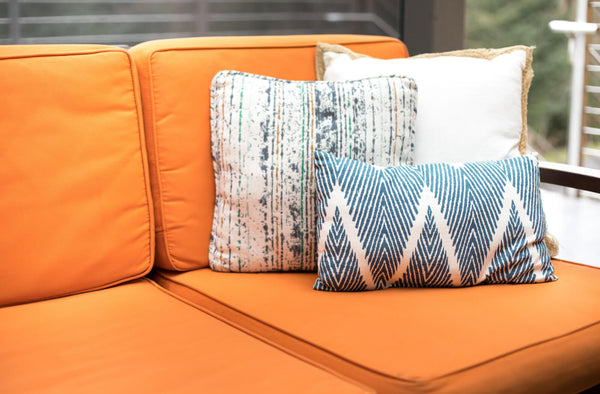Blue and white throw pillows in different sizes on an outdoor patio bench with orange seat cushions.