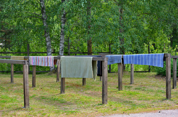 Rugs hanging on outdoor wooden drying racks set up over a lawn.