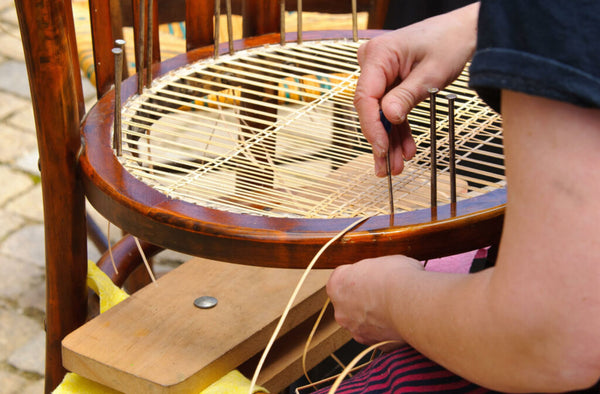 A man fixing a wicker chair by adding new strands