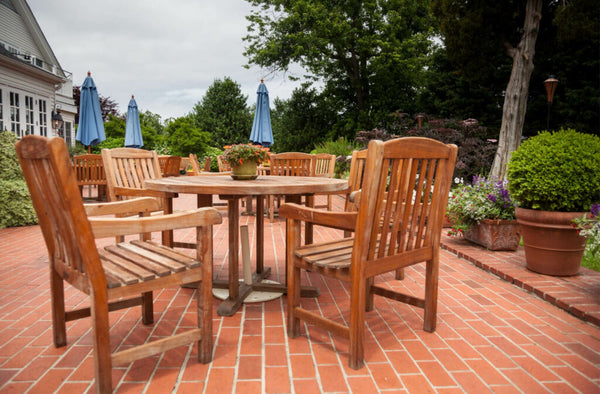Wooden teak tables and chairs on the brick patio. Teak holds a natural oil content that keeps it nourished and it naturally protects itself from weather and water.