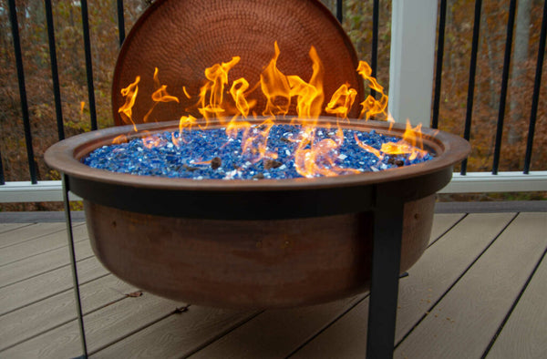 A copper fire pit sitting on a patio while lit to keep the patio warm and cozy