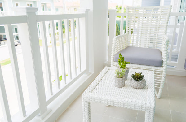A white resin table wicker and chair on a terrace with  ornamental plants in a white pot.