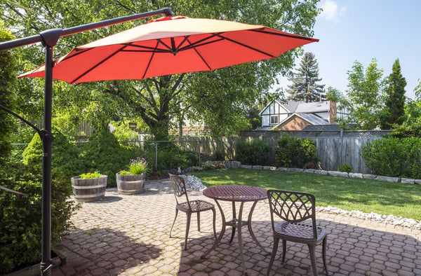 Cantilever orange umbrella shading bare patio furniture with greenery behind