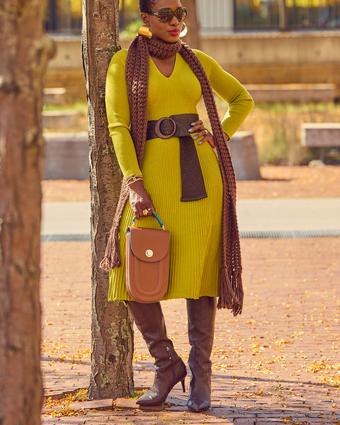 Fashion blogger Farotelle wearing a midi green sweater dress with a wide brown belt, a brown crochet sweater, and brown tall boots. She's holding a brown leather handbag and wearing sunglasses.
