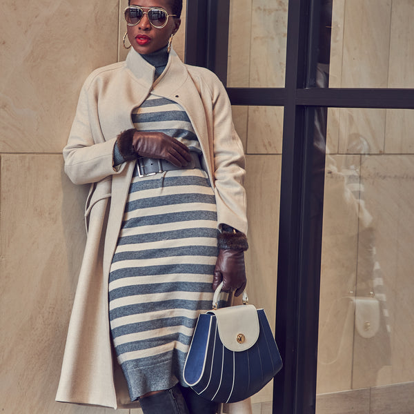 Fashion blogger Farotelle wearing a striped gray and beige sweater dress with a beige coat and a gray belt. She is also wearing brown leather gloves.