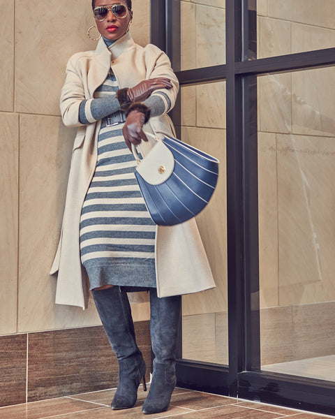 Fashion blogger Farotelle wearing a striped gray and beige sweater dress with a beige coat, a gray waist belt, and gray tall boots. She is also wearing sunglasses and brown leather gloves. She has a striped blue handbag.