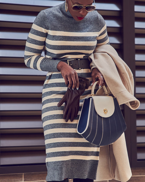 Fashion blogger Farotelle wearing a striped gray and beige sweater dress. She is holding a blue striped handbag.