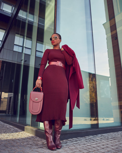 Fashion blogger Farotelle wearing a monochrome burgundy red outfit that consists of a burgundy sweater dress with a matching belt and matching tall boots. She is holding a bugundy rounded handbag.