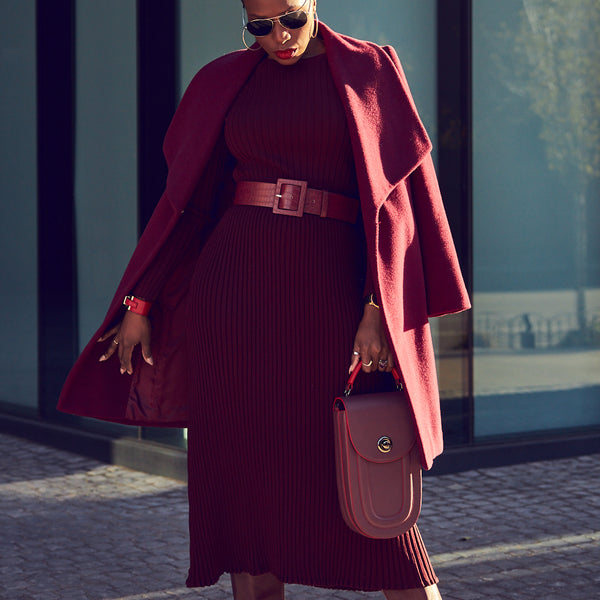 Fashion blogger Farotelle wearing a monochrome burgundy red outfit that consists of a burgundy sweater dress with a matching belt and a matching wool coat. She is holding a bugundy rounded handbag.