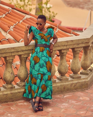 Style influencer Farotelle wearing a colorful Summer maxi dress. The dress has flutter sleeves and a shell-patterned print in turquoise and brown. She completed the outfit with chunky black sandals by Vagabond and a black waist belt.