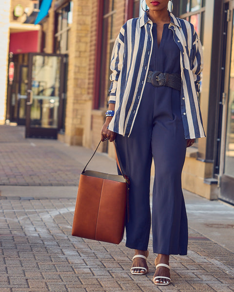 Farotelle wearing Ann Taylor blue belted sleeveless jumpsuit with H&M striped shirt, Schutz Ully sandals and Banana Republic Vida leather tote as Spring Summer elevated casual weekend style.