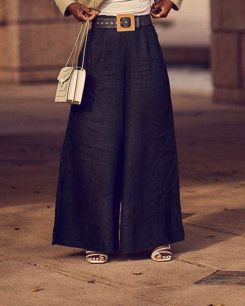 Style influencer Farotelle wearing belted wide-leg black pants with white strappy sandals and a rectangular white handbag.