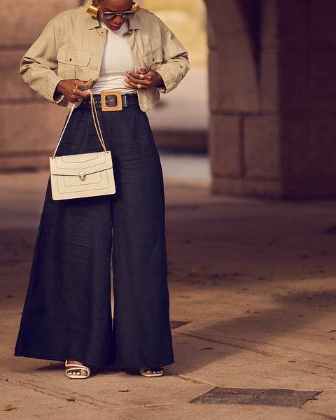 Style influencer Farotelle wearing wide-leg black pants with a fitted white tee and a cropped khaki jacket. She's also wearing sunglasses, white strappy sandals and is holding a rectangular white handbag. The outfit has a neutral color-blocked vibe.