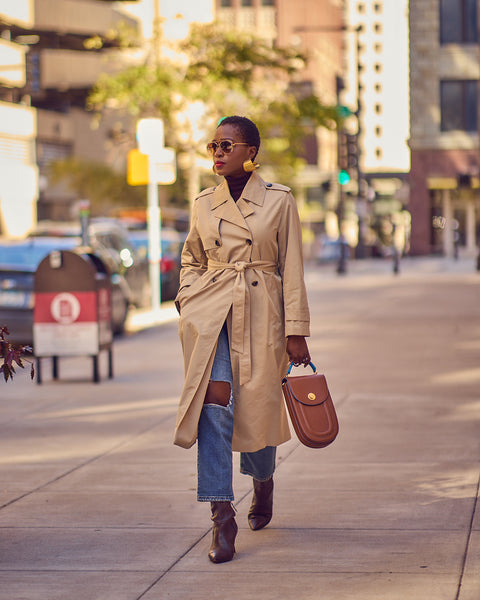 A woman wearing a light beige classic trench coat with distressed blue jeans and boots.