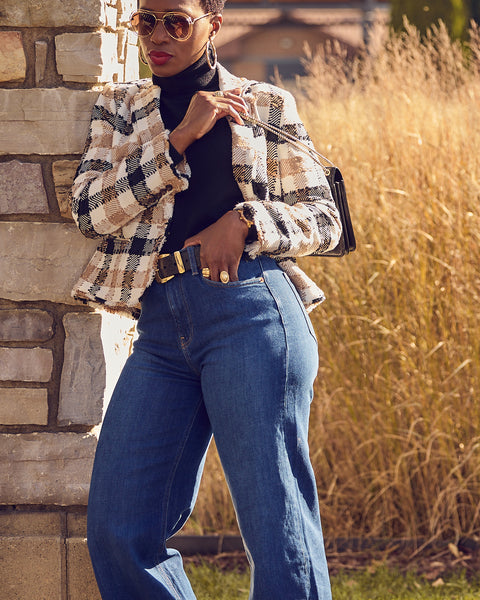 A woman wearing blue jeans with a black turtleneck and plaid cropped blazer. She is wearing black heels.