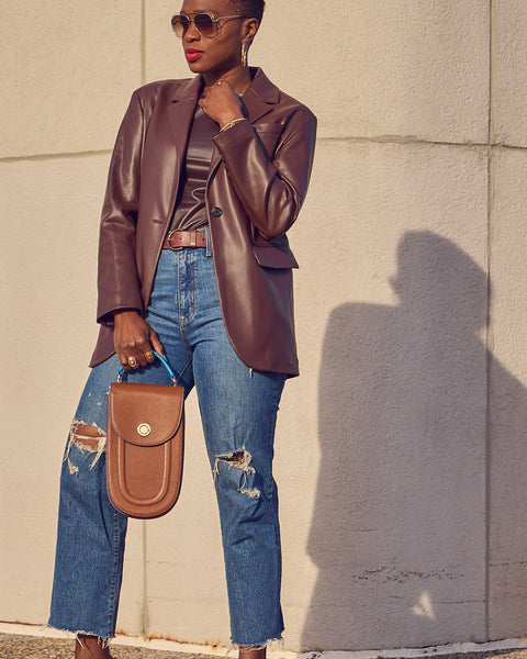 Style blogger Farotelle wearing blue jeans with a brown faux leather blazer over a brown faux leather fitted top. She is holding a brown leather handbag.