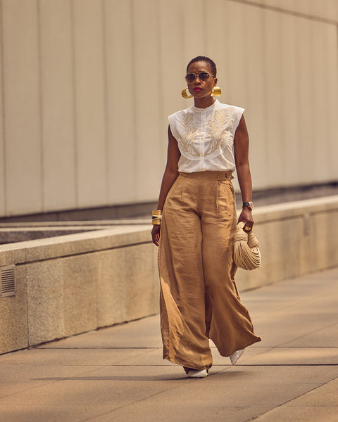 Style influencer Farotelle walking on a street and wearing a neutral outfit consisting of brown wide-leg pants, a white short-sleeve shirt, and a beige bag.