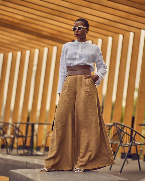 Style influencer Farotelle posing in a neutral outfit consisting of brown wide-leg pants, a white long-sleeve shirt, and a wide brown belt.