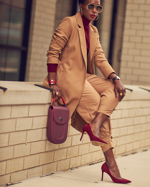 A fashion and style editorial photo showing influencer Farotelle wearing a color-blocked office outfit. She is wearing khaki pants with a matching camel-colored coat and a burgundy turtleneck sweater. She is also wearing Burgundy suede pumps. 