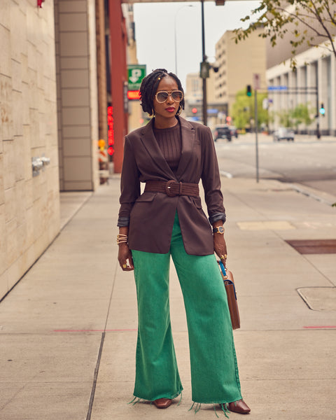 Fashion influencer Farotelle wearing green wide leg jeans with a brown belted blazer. She's posing in a city street.