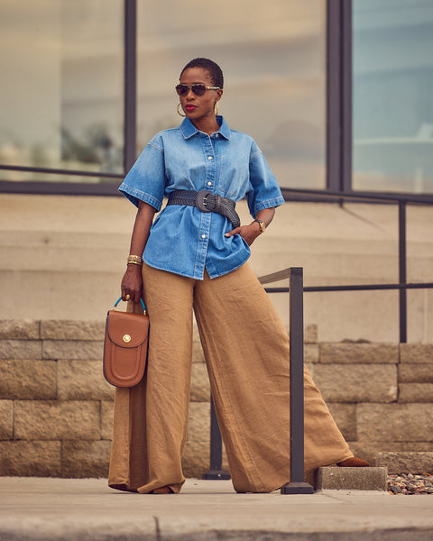 Style influencer Farotelle wearing Banana Republic khaki wide-leg linen pants with a belted denim shirt and brown pumps. She is holding a brown handbag and wearing sunglasses.