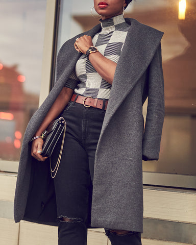 A close-up photo of a woman wearing black slim jeans with a grey checkered sweater and a grey coat. This is a neutral outfit idea for Fall and Winter.