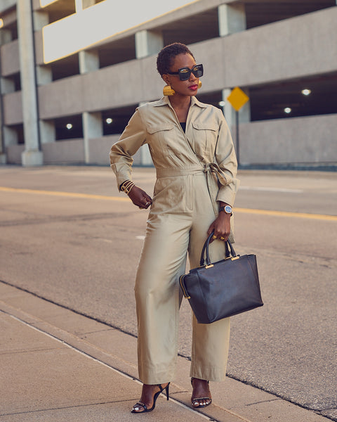 Farotelle wearing neutral Banana Republic utility jumpsuit, Amazon sunglasses, large gold earrings, Coach dress sandals and holding black leather tote bag as Business Casual Spring Summer Workwear Outfit.