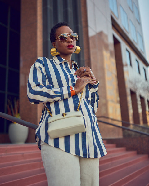 Style influencer Farotelle wearing an elevated casual Spring outfit. The outfit consists of an oversized striped button-down shirt with light denim culottes. She is wearing a chain crossbody bag.