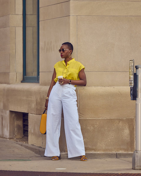 Style Influencer Farotelle standing on a street and wearing a color-blocked outfit that consists of white pants and a yellow shirt.