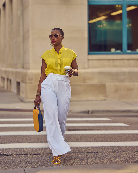 Style Influencer Farotelle walking on a street and wearing a color-blocked outfit consisting of white pants, a yellow shirt, yellow sandals and a yellow bag.