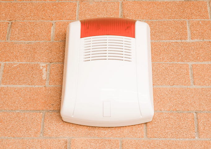 Red and white burglar alarm on a brick wall