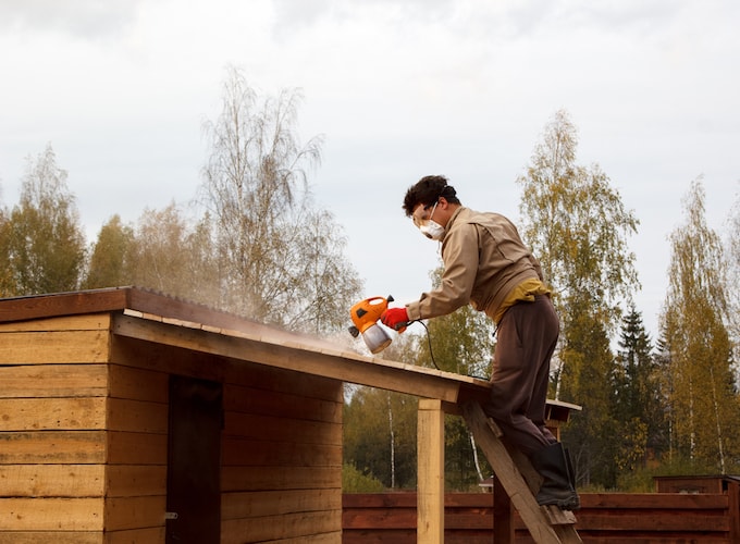 Man spraying waterproofing preservative on wooden structure