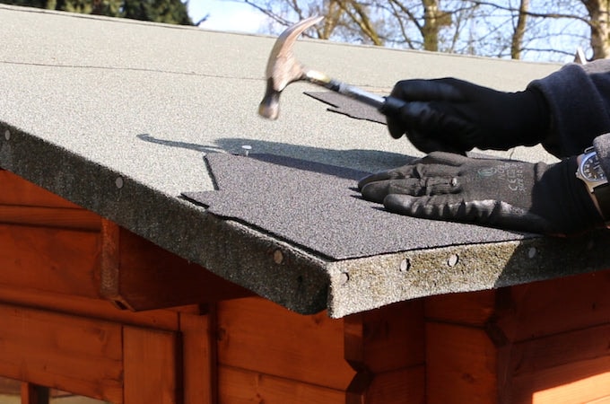 Person attaching first shingle strip to shed roof