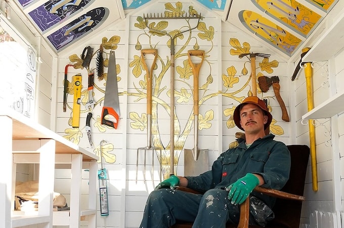 Artist sitting inside decorated shed studio