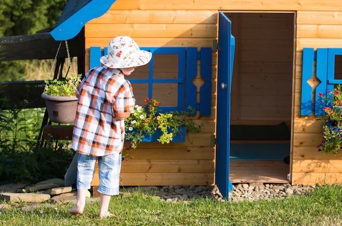 Child standing in front of wooden playhouse