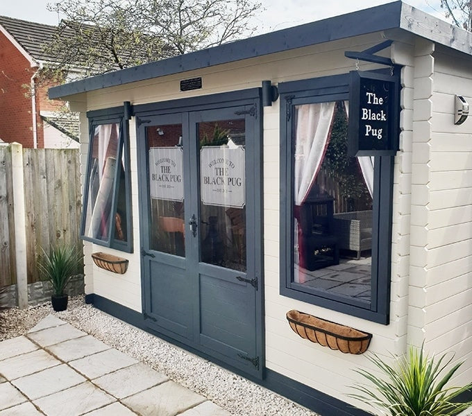 Front view of a painted log cabin pub called 'The Black Pug'