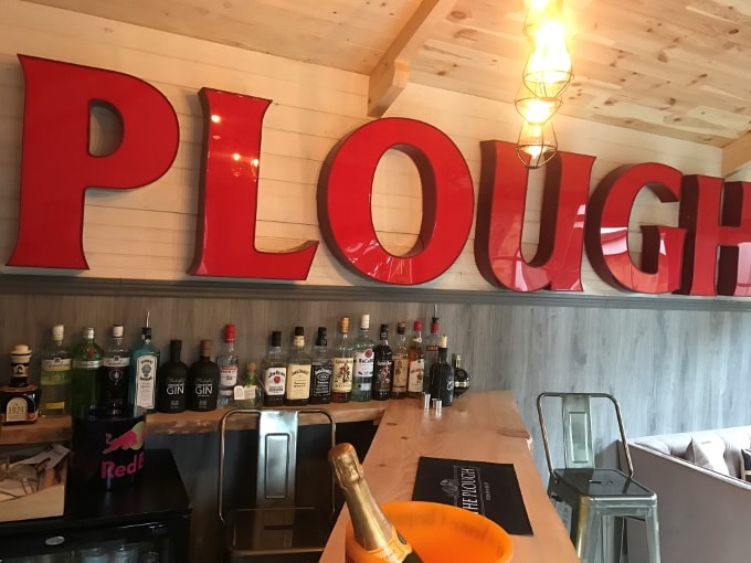 A well stocked man cave bar with a large red sign saying 'Plough'