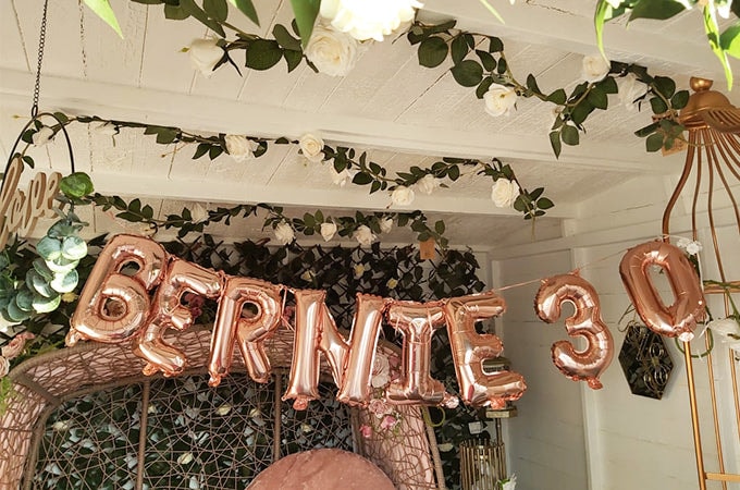 Rose gold balloons saying 'Bernie's 30th' against flower wall in Waltons summer house