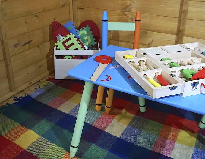 Interior of a wooden playhouse with a check print rug, colourful furniture and a toy box