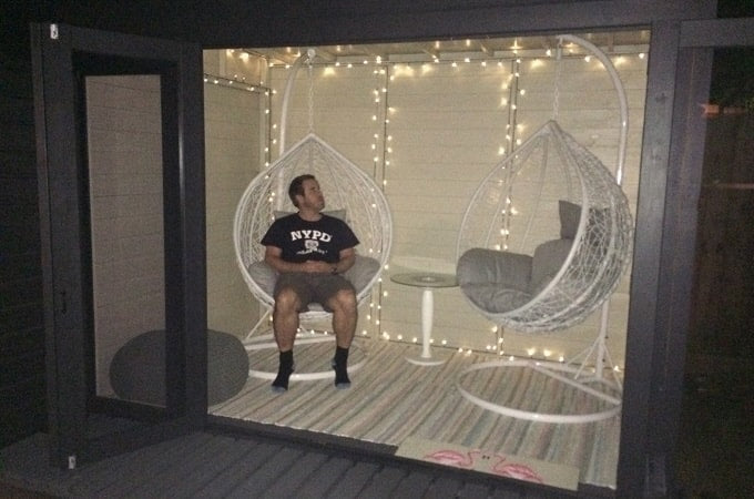 Man sitting inside Waltons summer house with fairylights and egg chairs
